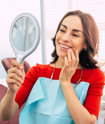 Woman admiring her smile in mirror after dental services in Melbourne