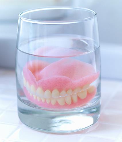 A set of dentures Melbourne soaking safely in a denture solution container