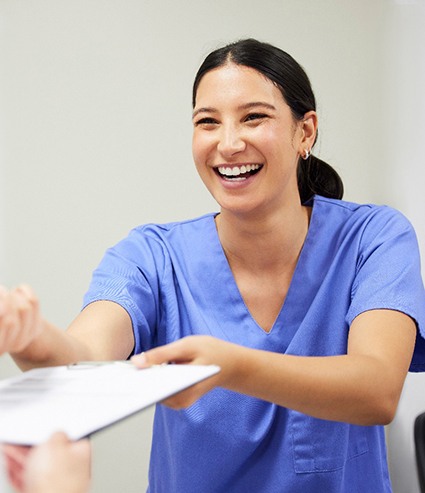 Smiling dental assistant handing patient form