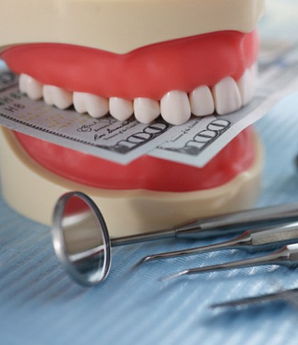 A jaw mockup biting hundred dollar bills next to dental tools