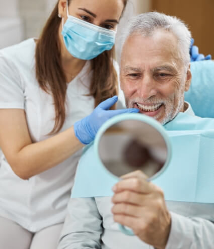 Older man seeing his smile in mirror at dental office