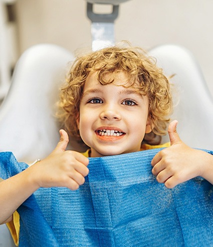 Child in dental treatment chair, making thumbs-up gesture