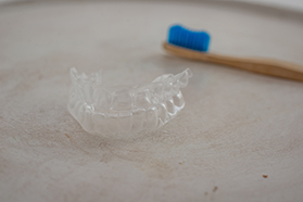 Blue-bristled toothbrush next to Invisalign on textured surface