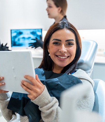 Patient smiling while holding mirror in treatment chair