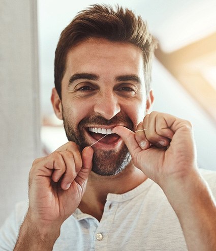 Man smiling while flossing his teeth in bathroom