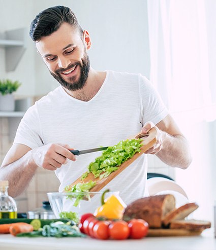 Man smiling while making salad in kitchen at home