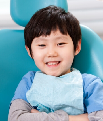 Smiling young boy in blue shirt sitting in dental chair