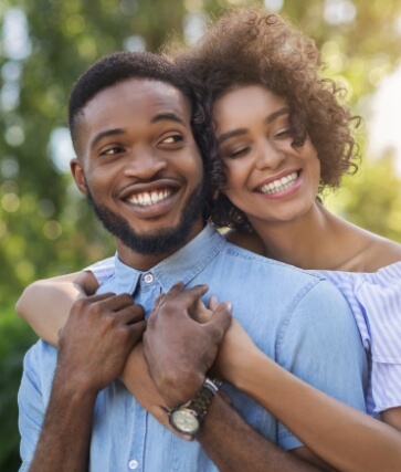 Young woman hugging young man from behind with trees in background