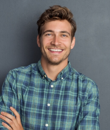 Young man in green plaid shirt smiling with arms crossed
