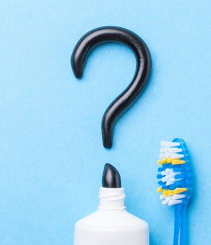 Charcoal toothpaste making a question mark on blue background next to toothbrush