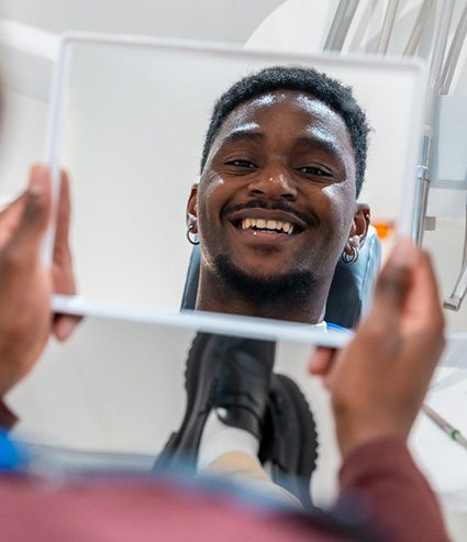 Man smiling at reflection in handheld mirror