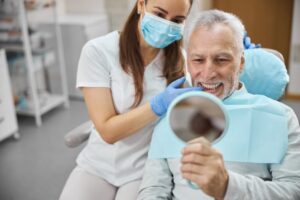 Older man smiling in mirror in dentist's chair.