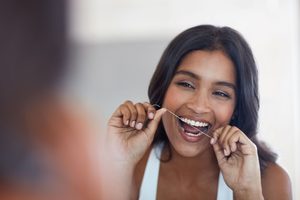 Woman flossing teeth in front of mirror